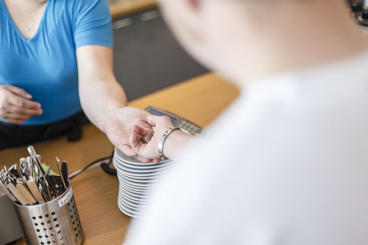 Maksutilanne kahvilassa. Asiakas ojentaa kolikoita myyjän käteen.