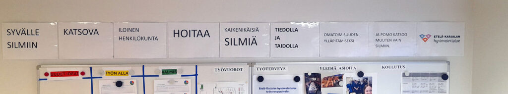 Taulun yläosassa näkyy tekstiä, kuten "SYVÄLLE SILMIIN", "ILOInEN HENKILÖKUNTA HOITAA KAIKENIKÄISIÄ SILMIÄ" sekä "OMATOIMISUUDEN YLLÄPITÄMISEKSI". Tekstien alla näkyy osittain ilmoitustaulua ja sen sisältöä.